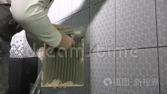 熟练的人在瓷砖上涂胶水，然后把它安装到墙上。 穿脏衣服的工人