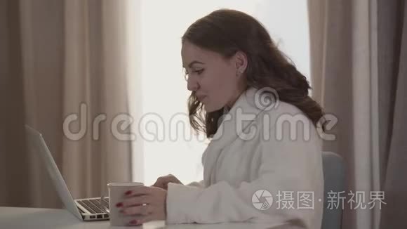 微笑的年轻女人使用笔记本电脑和喝咖啡的肖像。 美丽的黑发白种人女人享受沉默