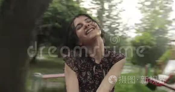 视频快乐迷人的女人在雨中的秋千上旋转。 有着深色短发的微笑女孩在这里玩得很开心