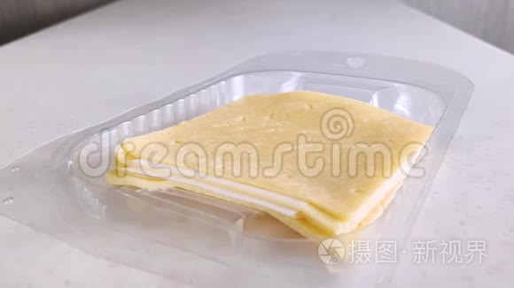 塑料包装中的方形黄色奶酪。 女白手拿一块.. 有小孔的切片奶酪