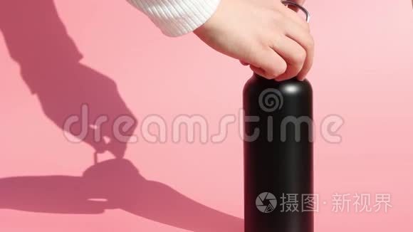 女性双手将可重复使用的金属瓶子，在粉红色背景下倒水