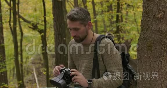 男性白种人游客坐在秋天的森林里，拿着相机说话。 自信的白发帅哥