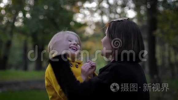 在秋天的公园里，有爱心和敏感的母亲和她迷人的微笑的女儿玩耍