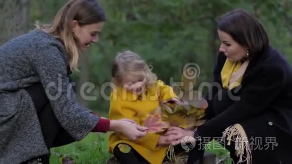 两个迷人的年轻女子和可爱的小女孩在公园的草坪上收集一束美丽的秋叶