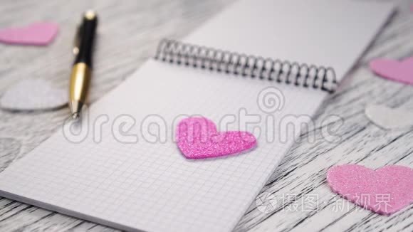 粉红色和白色的细纸心落在黑色金属装订的笔记本上