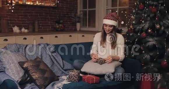 在舒适的圣诞节，戴着圣诞帽坐在圣诞树旁沙发上的年轻白种人微笑