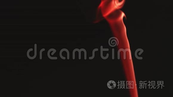 一股薄薄的红色烟雾在黑色背景下向上移动。 空间中缓慢运动的魔法雾