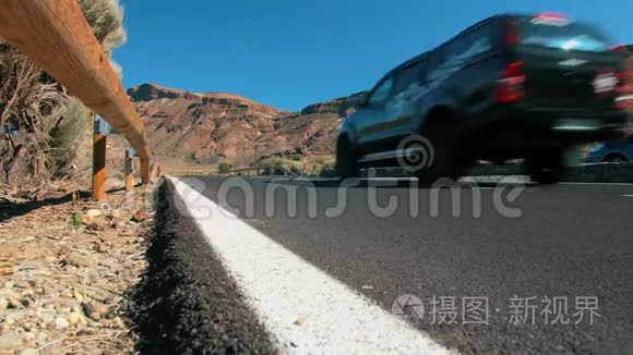 未被识别的黑色越野交叉车沿着沙漠中的一条山地沥青路行驶。 明亮的道路标记