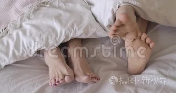 男性和女性脚躺在床单上的特写。 无法辨认的男人抓着腿，女人静静地躺着。 高级