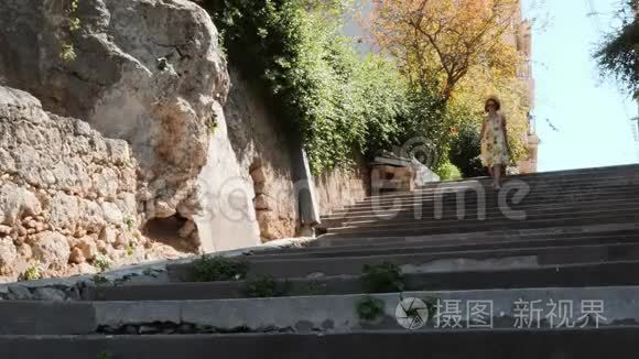 夏天穿着黄色礼服的迷人女子走在混凝土楼梯上，手拿着帽子，在原地旋转