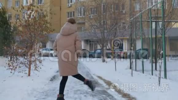 快乐的女人穿着米色羽绒服和柚子帽在雪城的冬天散步。 在雪地里跳舞的快乐女孩