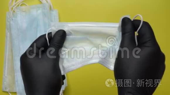 医生出示抗病毒口罩，手中拿着由黄色背景的黑色医疗手套保护的设备