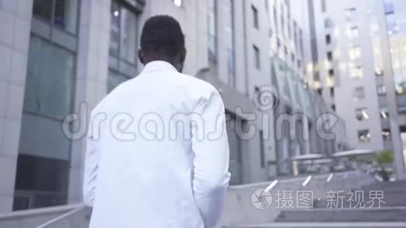 非洲裔美国人穿着白色衬衫朝大型现代商务中心走去。 男性商人或