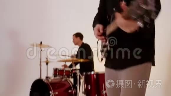 一支由四个人组成的音乐乐队在明亮的工作室里演奏歌曲-吉他手和鼓手用一个