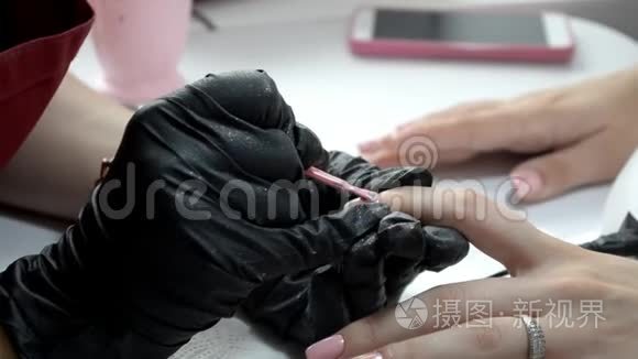 戴黑色手套的指甲油师傅在指甲上涂粉红色指甲油
