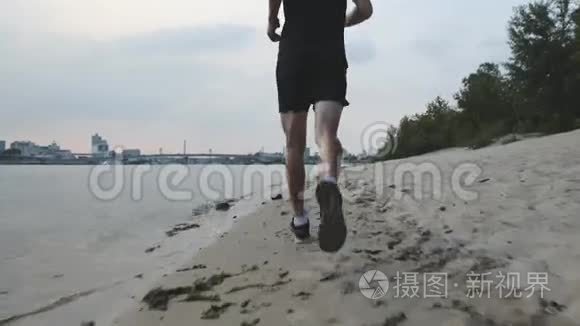 肌肉发达的雄腿沿着河滩奔跑。 晚上在河边慢跑的男腿。 附近有教养的男孩训练