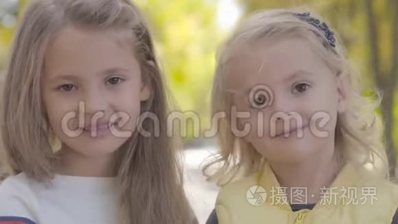 两个漂亮的小白种人姐妹站在秋天的公园里着的特写肖像。 美丽的微笑