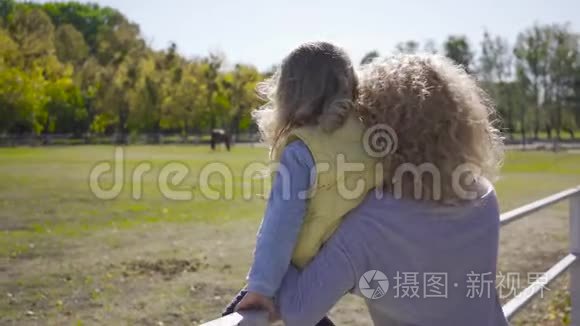 金发卷曲的白种女人和她的两个女儿看着背景上的马。高加索家族