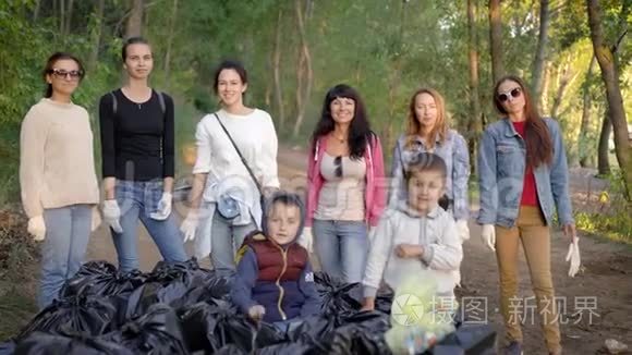 妇女和孩子们在林地的垃圾堆旁，用手指摆出胜利的手势，快乐而欢快