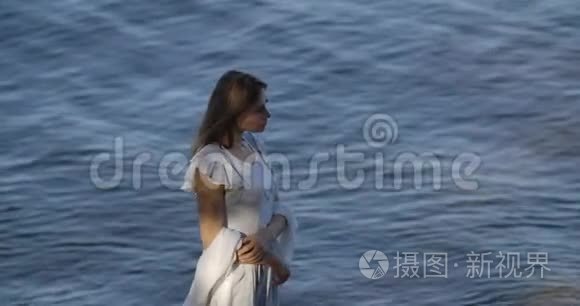 一位美丽的白种人女子站在海浪和思考的背景上，穿着浅白的裙子