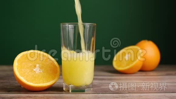 新鲜的黄色果汁被倒入一个高大的玻璃上的木制桌子，橘子在绿色的背景。