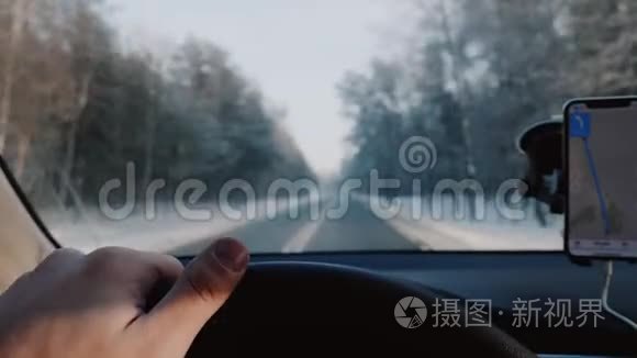 特写司机手握汽车方向盘在冬季道路上驾驶，智能手机导航应用程序慢动作。