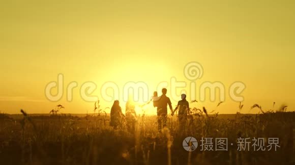 幸福童年的概念.. 幸福的大家庭在夕阳下穿过田野。 父母和三个孩子走进来