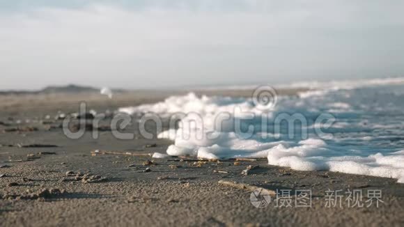 在晴朗的晴天，北海海滩上，在强风下，厚厚的白色海洋泡沫摇动的特写背景缓慢运动。