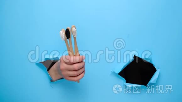 合拢雌性的手做拇指向上的手势，演示竹生态牙刷穿过撕裂的蓝色纸墙。