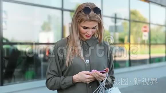 时尚的年轻女性，带着购物袋，微笑着用智能手机在户外聊天