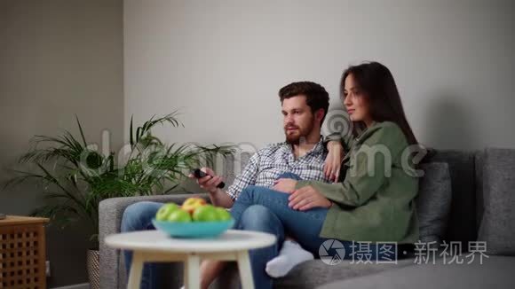 年轻可爱的白种人夫妇在客厅沙发上看电视的画像