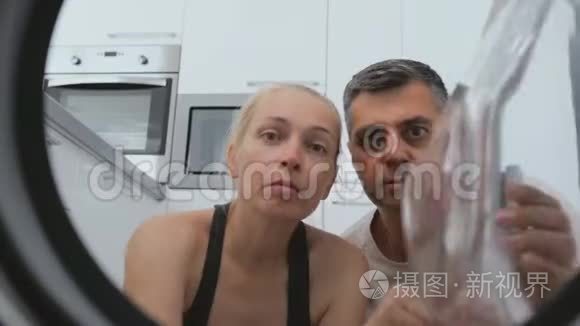 一个女人和一个男人坐在洗衣机前面，惊讶地看着里面的鼓。 拍摄是从