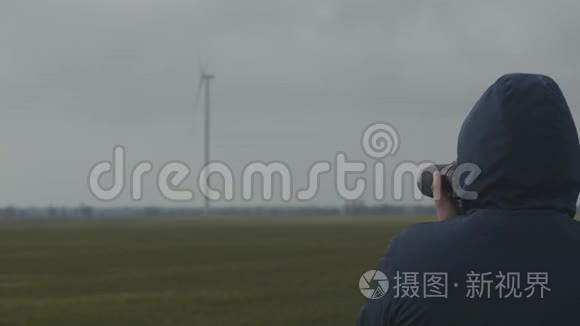 在一个多云的日子里，一个职业摄影师在一个野外拍摄旋转风力发电机的照片。