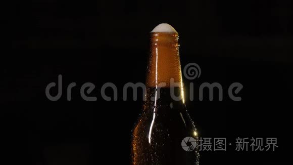 一瓶啤酒被一只雄性的手打开。 一瓶啤酒，在黑色背景特写上滴着水。