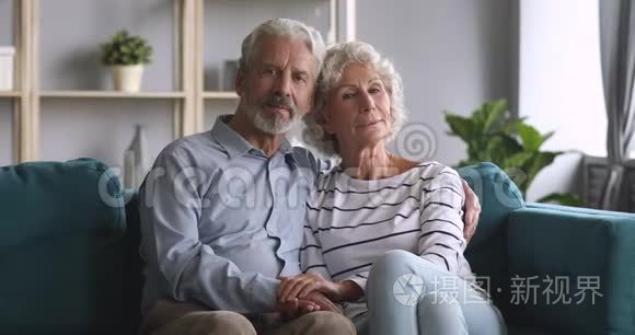严肃快乐的老夫妇在沙发上看着摄像机