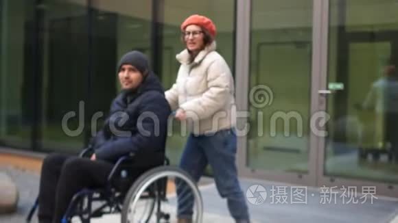 女人带着一个年轻人坐轮椅。 一对年轻夫妇穿着秋天的夹克和帽子。 残疾人及其