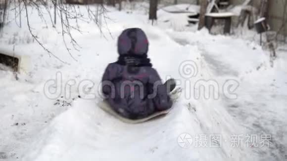 一个孩子在雪地滑梯上翻滚。 冬天在街上玩。 在寒冷的冬天，孩子穿着一件夹克和一件