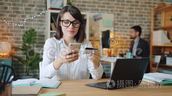 年轻妇女在工作中使用信用卡和智能手机在线支付