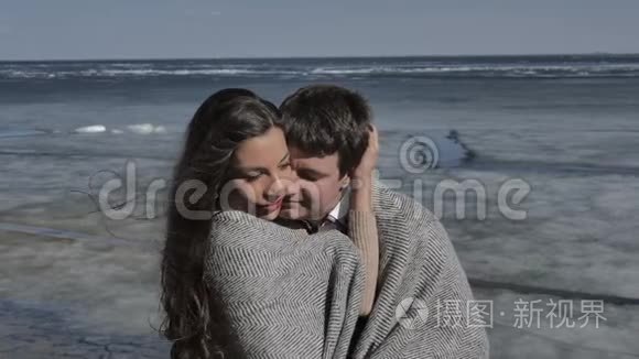 年轻夫妇拥抱着，背景是一条覆盖着冰的河流，阳光明媚的春天