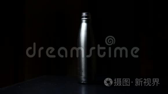 特写可重复使用的钢制热生态水瓶和盖子，黑色背景。