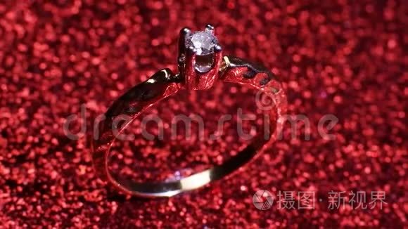 美丽闪亮的金色订婚戒指与大宝石钻石在闪光的红色背景。 情人节`礼物。