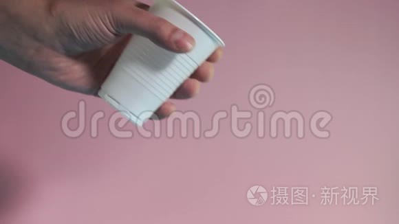 手在粉红色的背景上扔出一个塑料杯。 环境污染问题。 对塑料的排斥