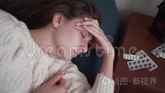 一个发烧头痛的病妇躺在床上，看着药丸和药物的包装。 强烈的偏头痛和
