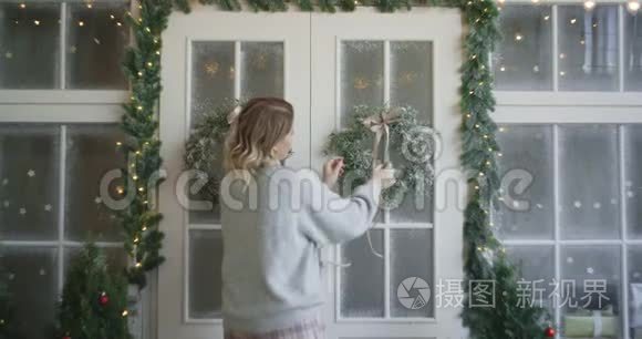 穿暖和毛衣的女人用圣诞花环装饰大门，装饰圣诞屋，舒适的新房子