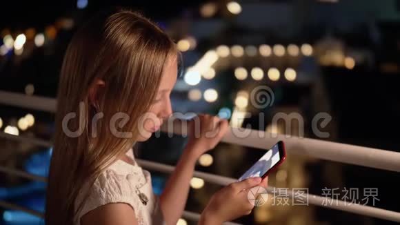 年轻女孩在黑暗阳台上的社交网络中看智能手机在线广播。 使用手机的少女
