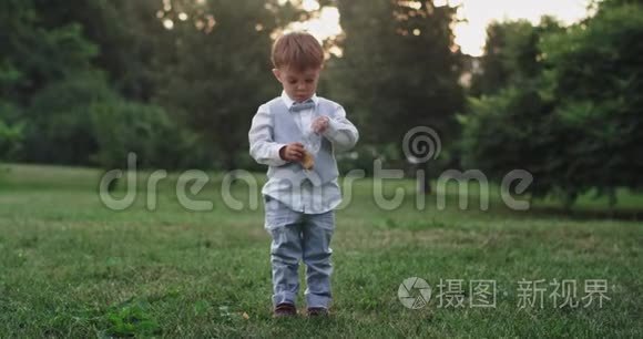 可爱的小男孩穿着休闲服，在公园中央的镜头前吃着零食