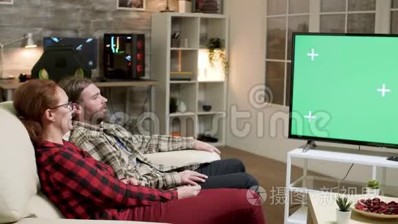 hipster夫妇坐在电视机前的沙发上，屏幕是绿色的