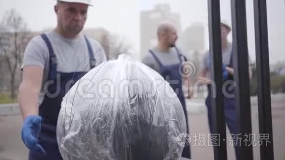 成年白种人，戴着白色头盔和制服，带着包裹步行到大楼。 上班的肌肉接生员