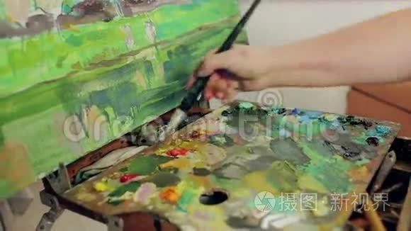 一个女人用调色板和画笔用油画颜料描绘风景。 投中弹