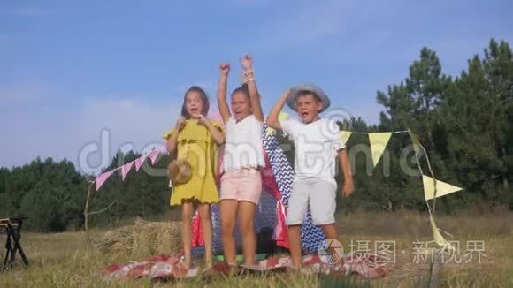 孩子们在野餐中玩得很开心，快乐的朋友们在户外活动时，在wigwam的背景下积极地跳舞和唱歌